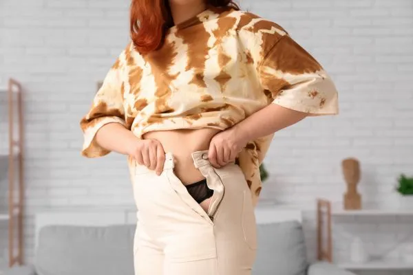 Image of woman trying to do her trousers up after pregnancy weight gain Thrapston